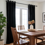 Black grommet curtains hanging on a window in a dining room with a wooden table and chairs.