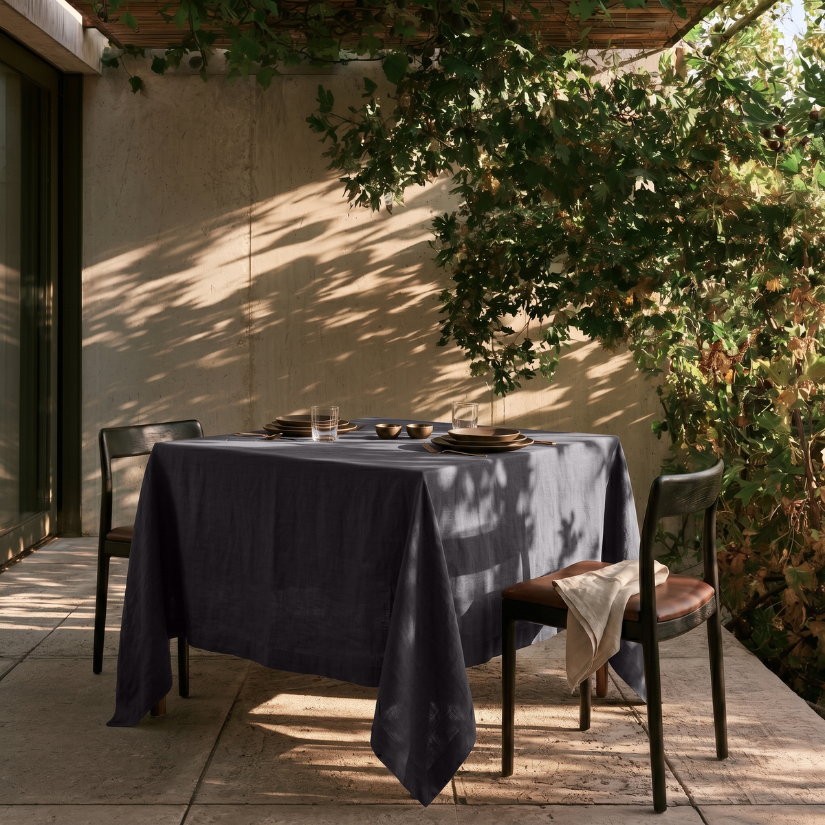 Charcoal Grey Square Linen Tablecloth on a Contemporary Outdoor Patio with Concrete Walls and Lush Greenery