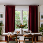 Inviting dining room with deep red rod-pocket curtains, wooden furniture, and fresh greenery