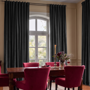 Elegant dining room with dark curtains, red velvet chairs, and a wooden table.