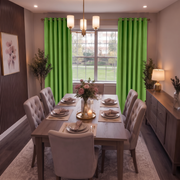 A styled dining room featuring a wooden dining table surrounded by tufted beige chairs, set with plates and a floral centerpiece. The room has bright green curtains, a wood sideboard, and a window looking out onto a green lawn.