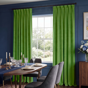 Bright green pleated curtains hanging on a dark wood rod in a dining room with blue walls, a set dining table, chairs, and a window view.