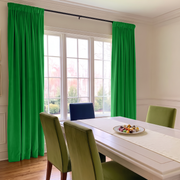 Bright dining room with bright green curtains hanging on a black rod over a multi-pane window, with a white dining table and green chairs in the foreground.