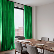 Bright green pleated window curtains hanging on a black rod in a modern dining room with a wooden table and gray chairs.