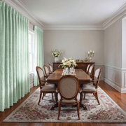 A styled dining room featuring a dark wood rectangular dining table surrounded by six upholstered chairs with cream fabric and curved backs. The set is arranged on a large, ornate floral patterned area rug over hardwood floors.