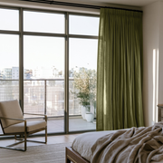 Olive Green Linen Pencil Pleat Bedroom Curtains in an Airy Contemporary Bedroom with Minimalist Lounge Chair with Soft Neutral Accents