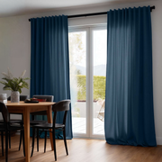 A pair of deep blue grommet-top curtains hanging on a black rod over a sliding glass door in a modern dining room with a wooden table and chairs.