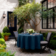 Peacock Blue Linen Round Tablecloth in an Outdoor Courtyard Dining Setting with White Brick Walls and Black Metal Accents