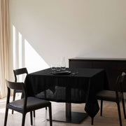 Black Square Linen Tablecloth in a Minimal Dining Room with Cream Walls and Dark Wood Chairs