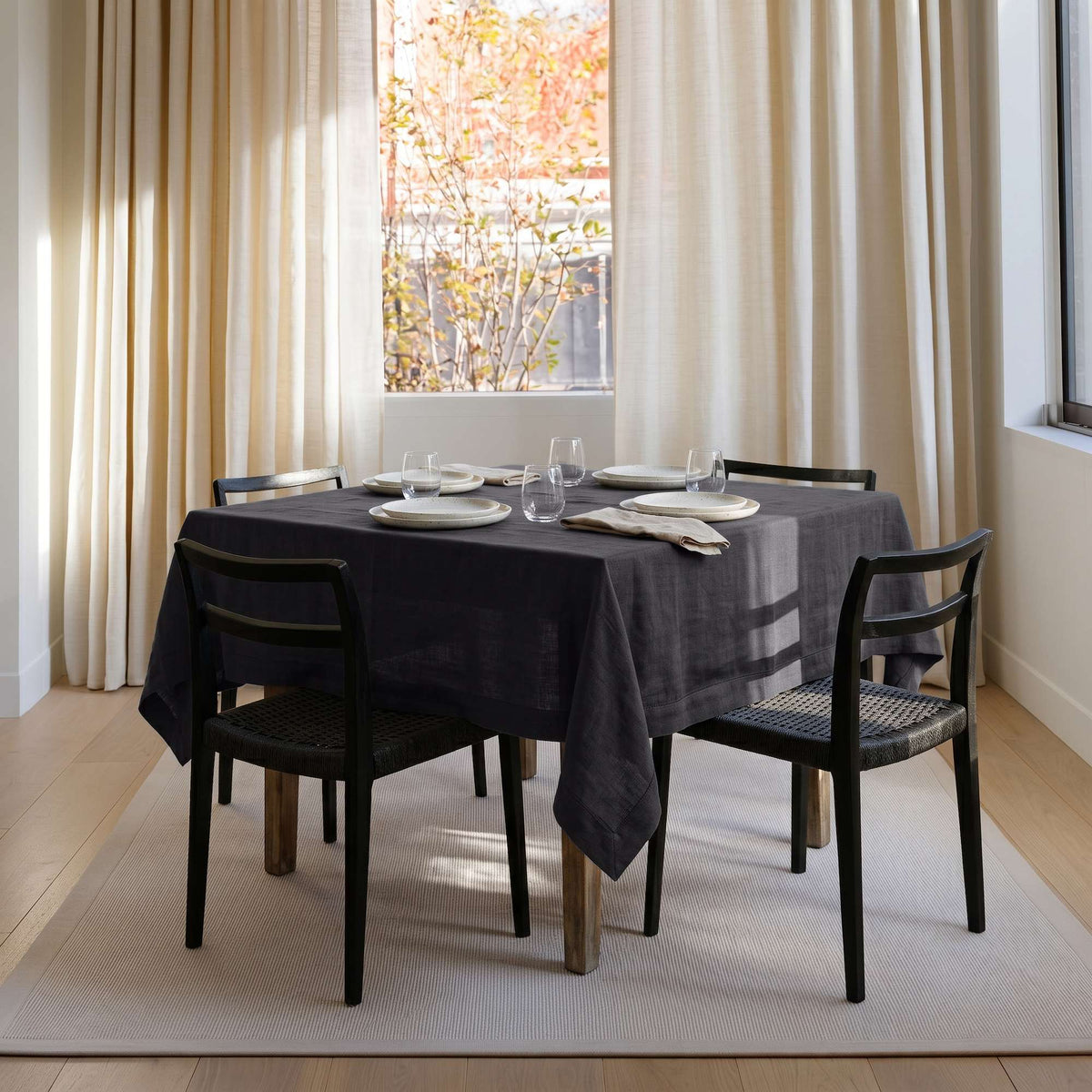 Charcoal Grey Square Linen Tablecloth in a Bright Contemporary Dining Room with Black Chairs and Cream Curtains