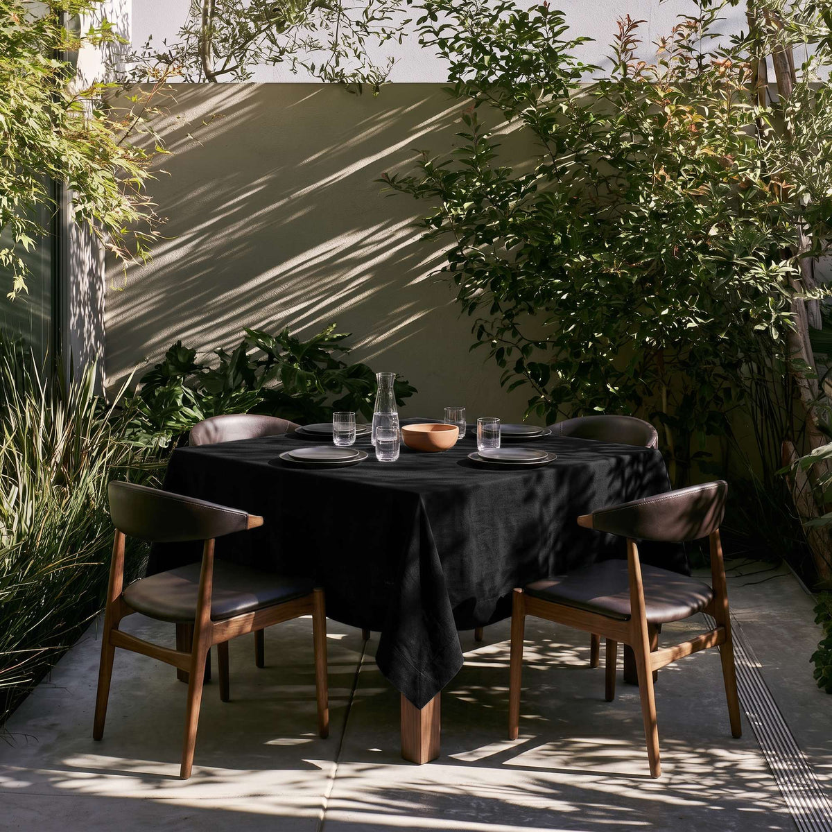 Black Square Linen Tablecloth on a Contemporary Garden Patio with Lush Greenery and Wood-Framed Chairs