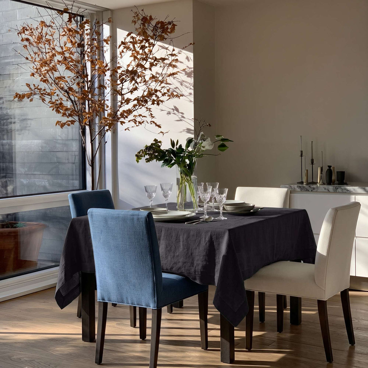 Charcoal Grey Square Linen Tablecloth in a Modern Dining Room with Blue Upholstered Chairs and Floor-to-Ceiling Windows