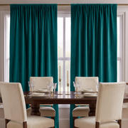 A pair of floor-length teal curtains hanging on a gold rod over two tall windows, with a dark wood dining table and cream upholstered chairs set in front.